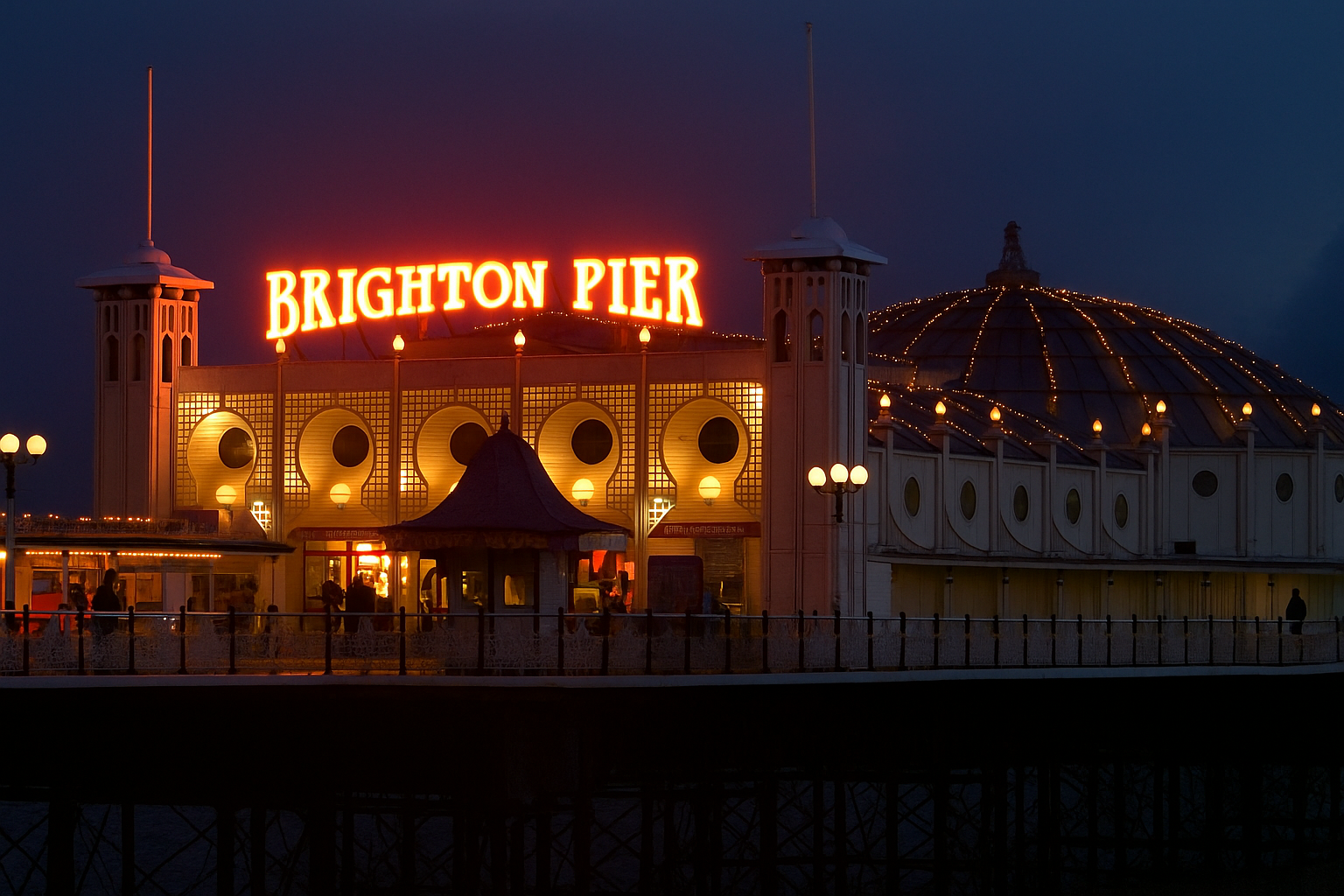 alt="glowing neon lights of Brighton Pier lighting up the seafront"